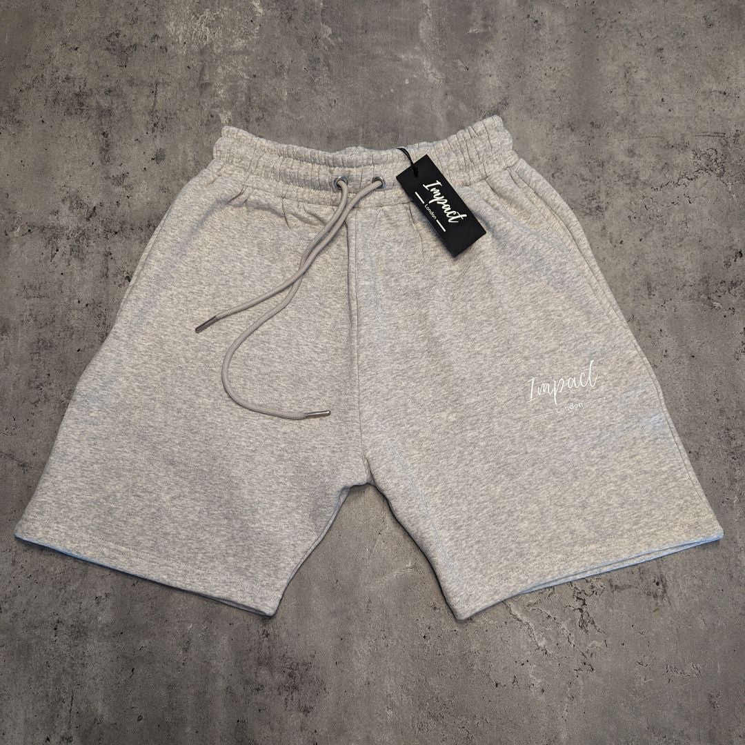 Front of men's grey jogger shorts with white Impact London logo on a light grey wooden background