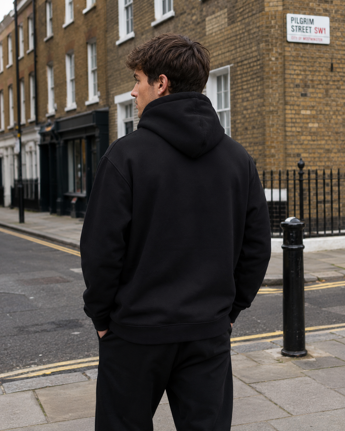 Male model wearing Impact London black hoodie with white embroidered logo from the back