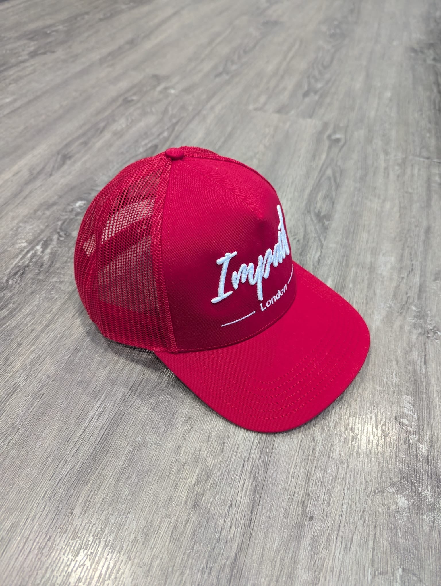 Red trucker cap with white logo from Impact London